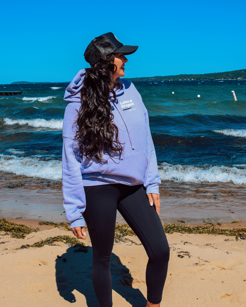In this image, we see a Lakes and Grapes Great Lakes Surf Hoodie. This sweatshirt, available in a cool dark lavender color, captures the spirit of the water like no other.