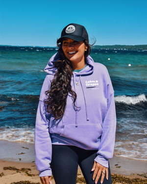 In this image, we see a Lakes and Grapes Great Lakes Surf Hoodie. This sweatshirt, available in a cool dark lavender color, captures the spirit of the water like no other. 
