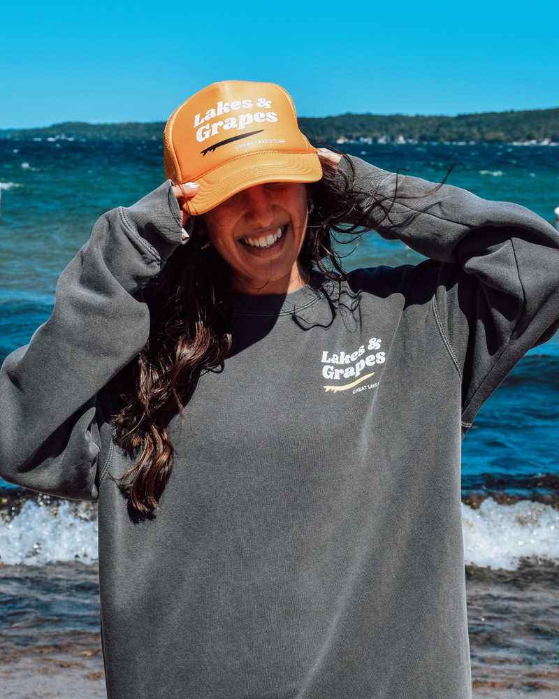 In this image, we see a Lakes and Grapes Great Lakes Surf Trucker Hat. Experience comfort and style as you embrace the spirit of the Great Lakes.