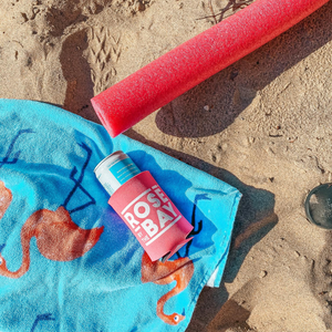 Pink Rosé by the Bay Koozie, Flamingo Towel, and Pink Noodle on the sandy beach in Traverse City