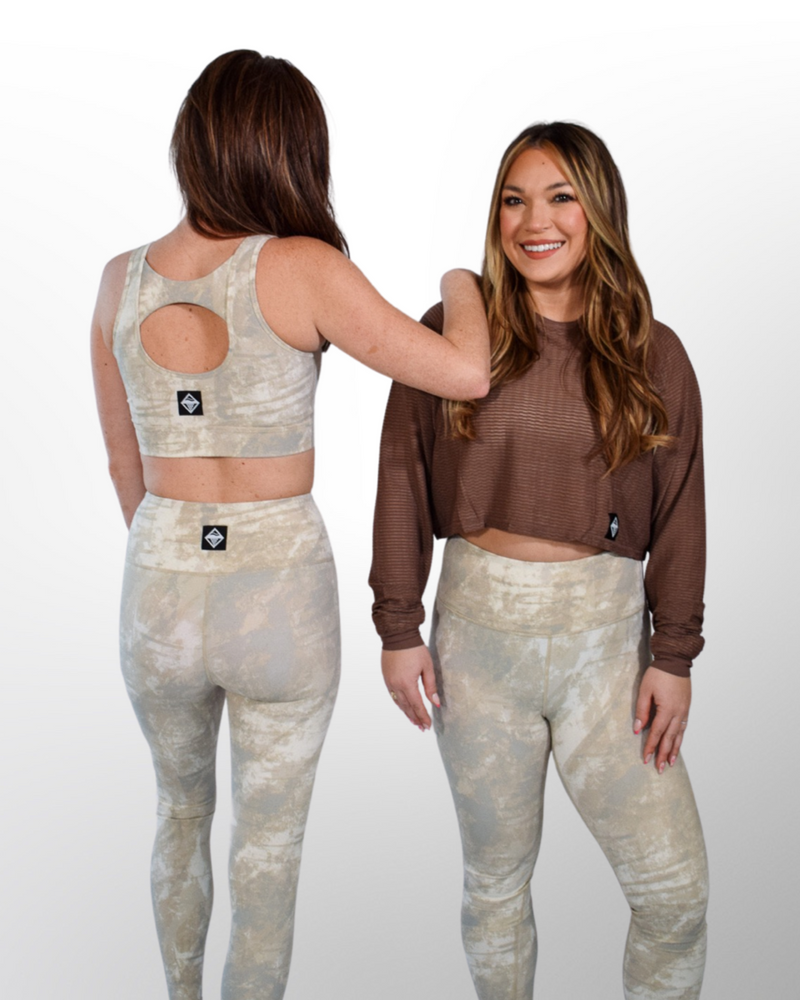The image showcases a Sand Tie Dye Sports Bra, a tie-dye pattern in soft sand tones, creating a unique and trendy design. The fabric appears stretchy and durable, offering support during physical activities.